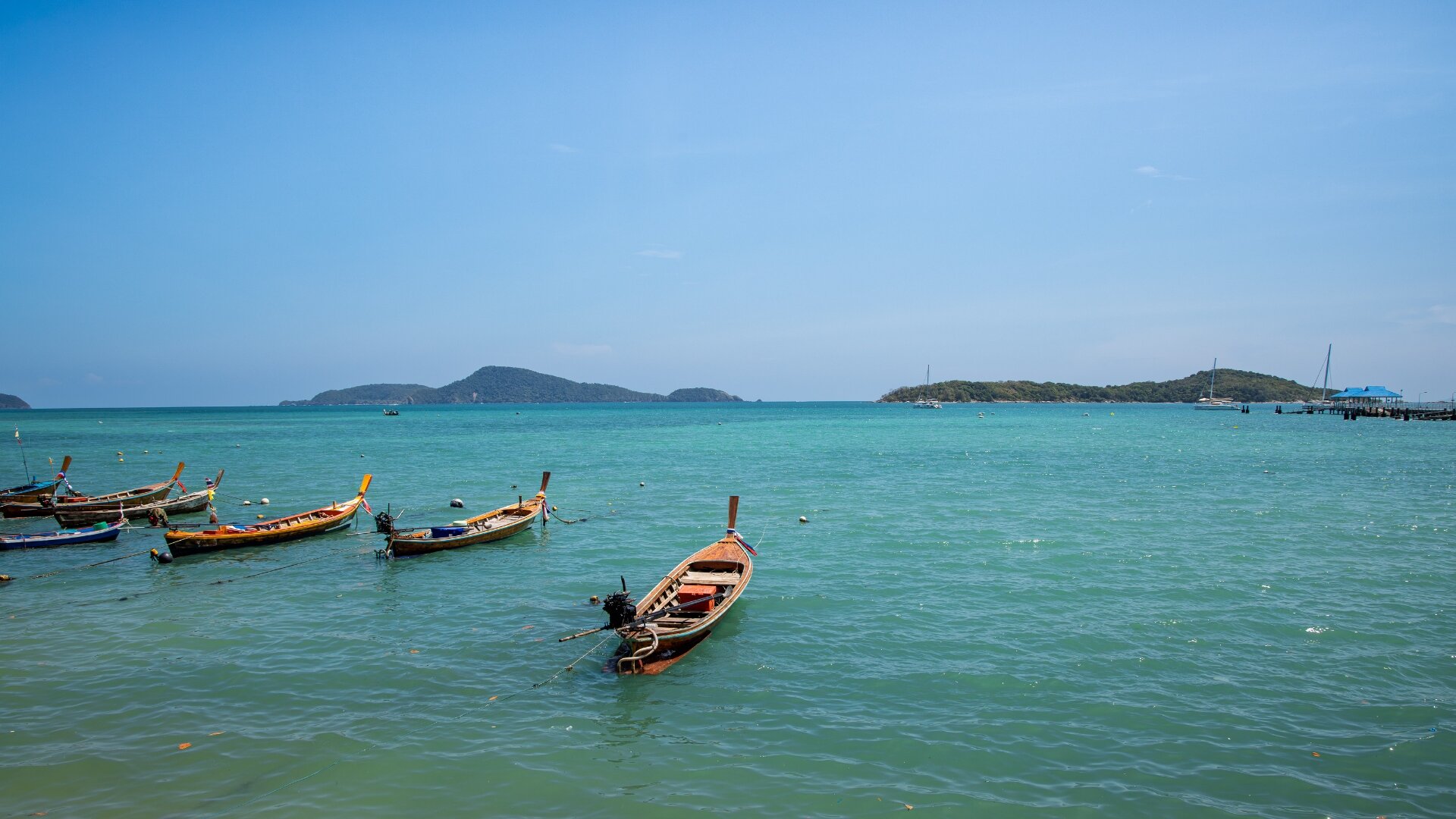 Wooden fishing boats and longtails moored in turquoise waters with green islands in the distance, Phuket — landscape photography