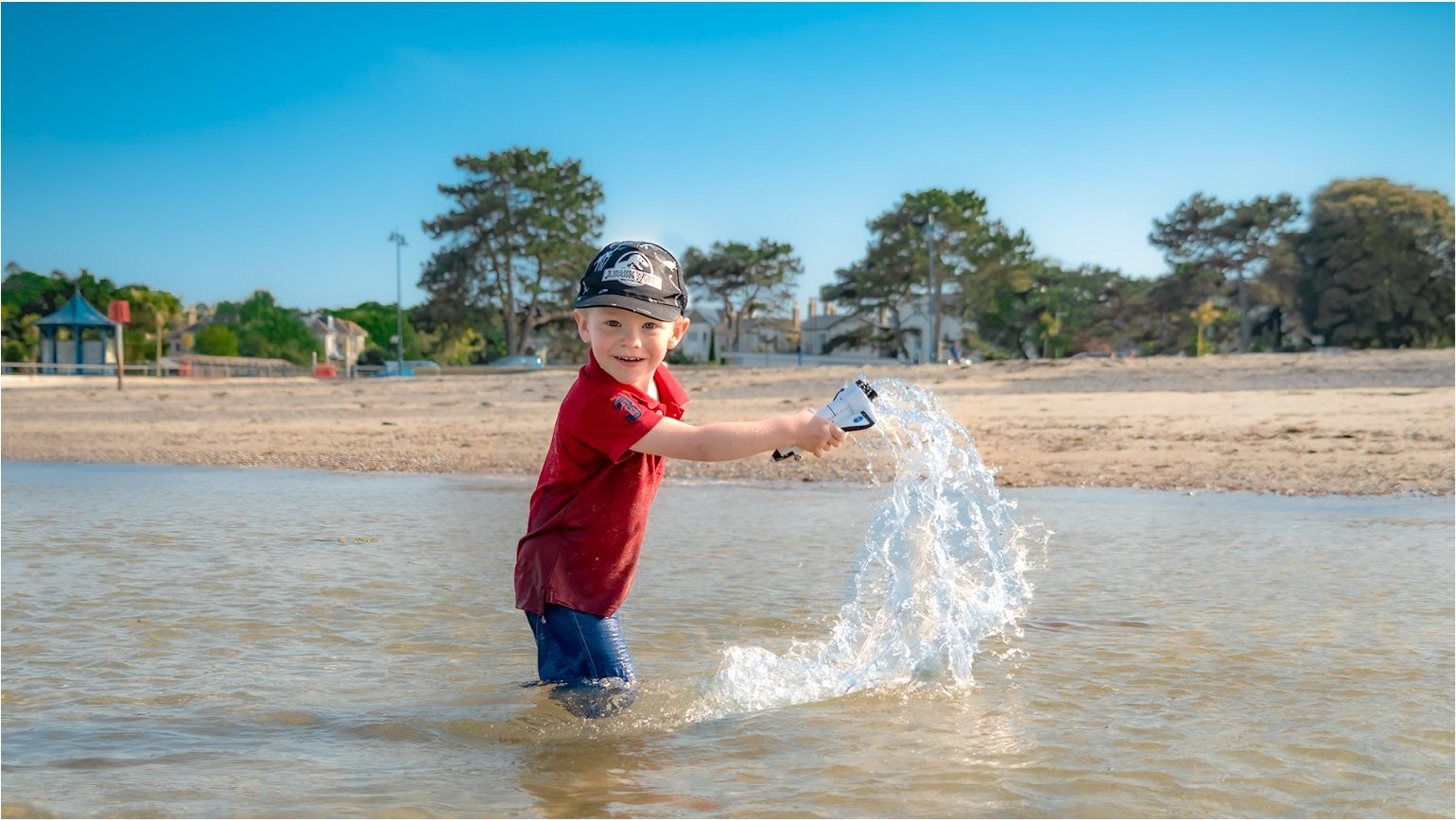 Child splashing in shallow water at beach with summer blue sky, Isle of Wight — lifestyle photography by Samuel John Ford