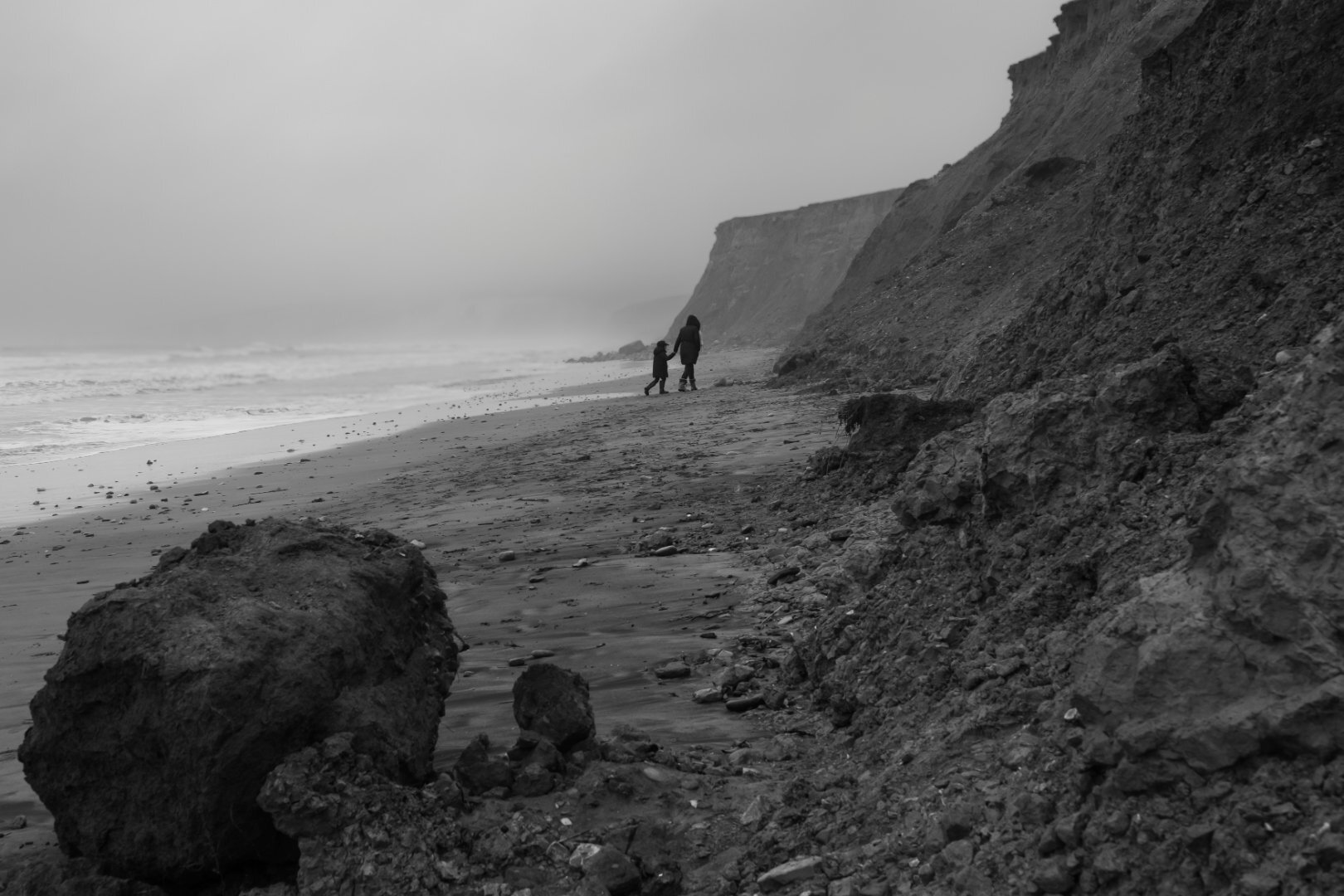 Black and white cliff walk with figures by eroding coastline and boulders, Isle of Wight — documentary photography by Samuel John Ford