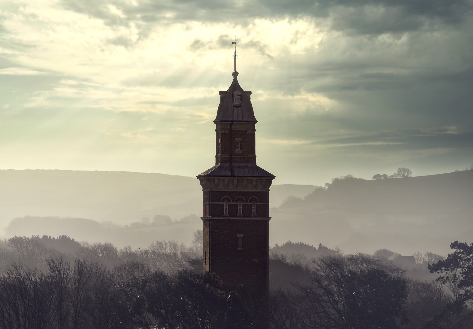 Victorian water tower silhouetted against dramatic clouds and misty downland, Isle of Wight — architectural landscape photography by Samuel John Ford