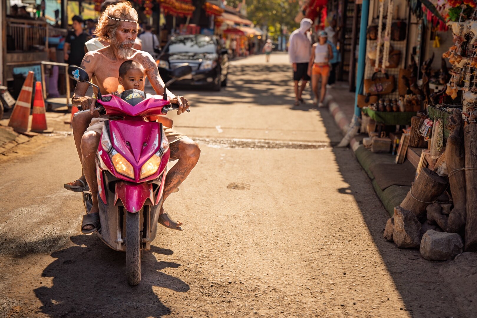 Man and child on a pink motorbike through golden-hour market street